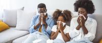family sitting together on a couch blowing their noses because they are sick